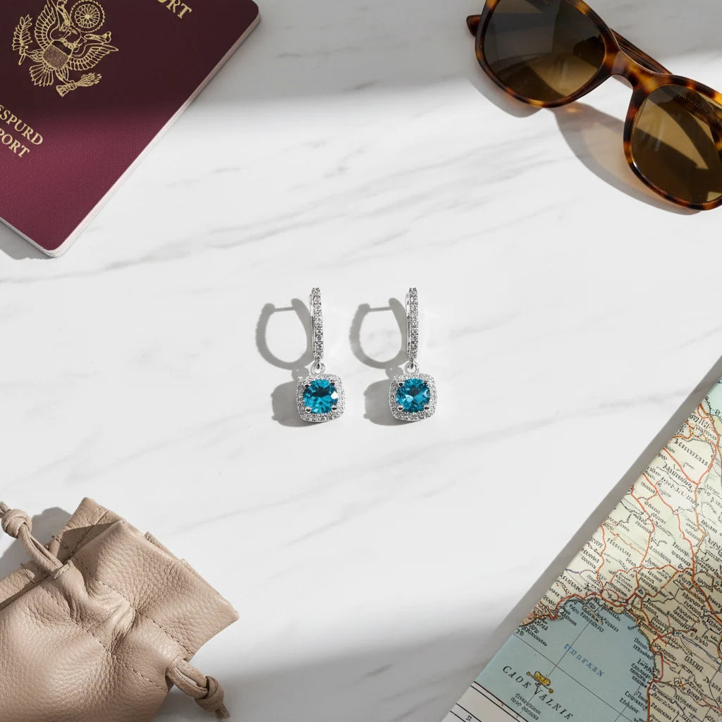 Aqua Blue Drop Huggie Earrings flat lay with passport, sunglasses, map, and pouch | OriaJewel