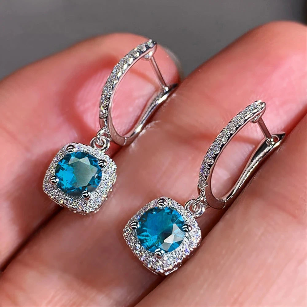 Aqua Blue Drop Huggie Earrings in-hand close-up showing huggie clasp and sparkle | OriaJewel