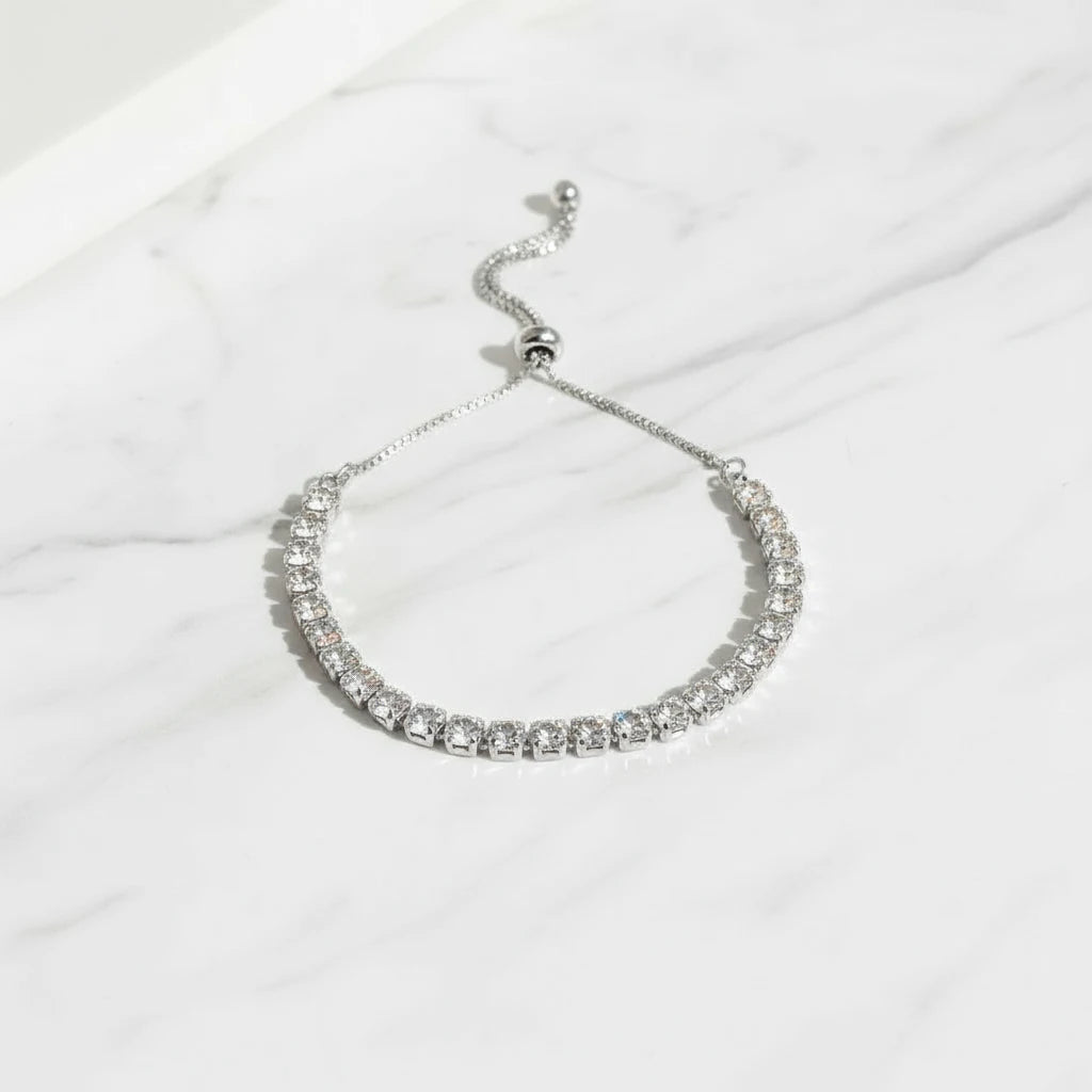 Close-up of a silver Aurelia Cluster Tennis Bracelet with sparkling round crystals arranged in a neat row on white marble, adjustable slider chain extended | Oria Jewel