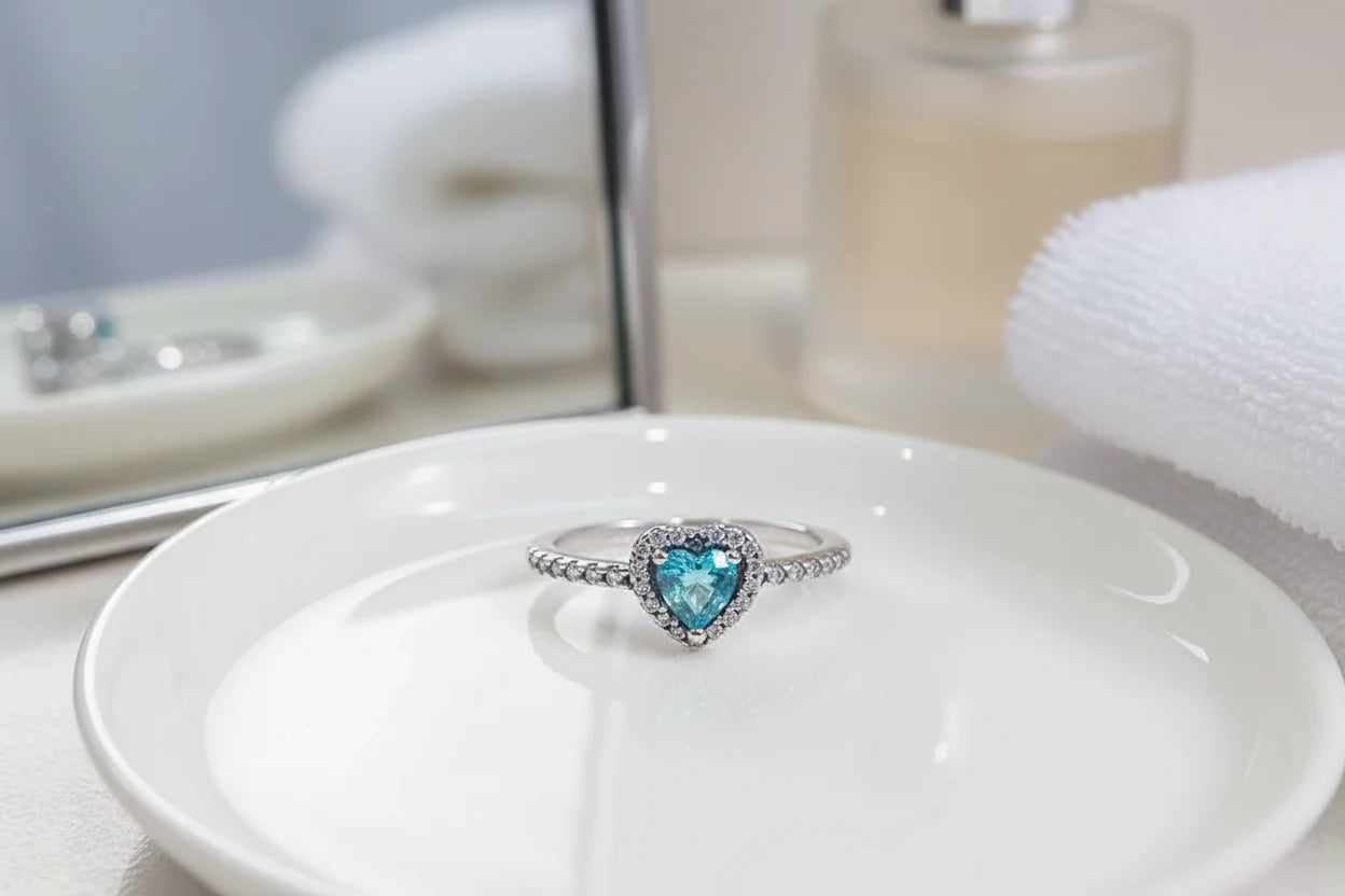 Blue Heart Halo CZ Ring close-up on a glossy white dish with a mirror and perfume bottle softly blurred behind, highlighting the blue heart gemstone, halo CZ border, and pavé-set silver band | OriaJewel