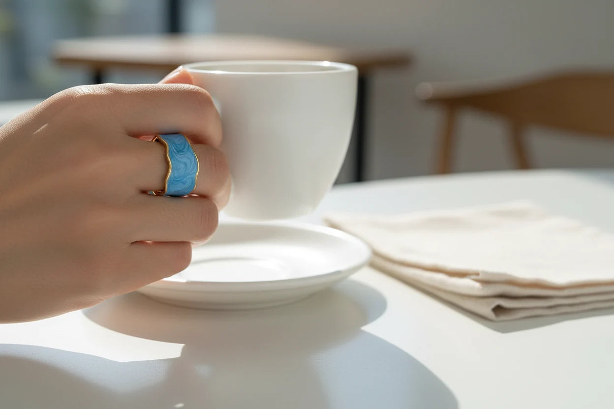 Close-up hand holding a white cup showing the Blue Marble Open Wave Ring with gold trim | OriaJewel