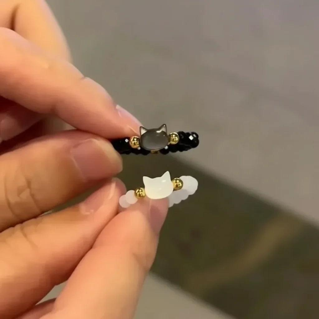Hands hold two beaded Cat Charm Rings, black and white with gold accents | Oria Jewel