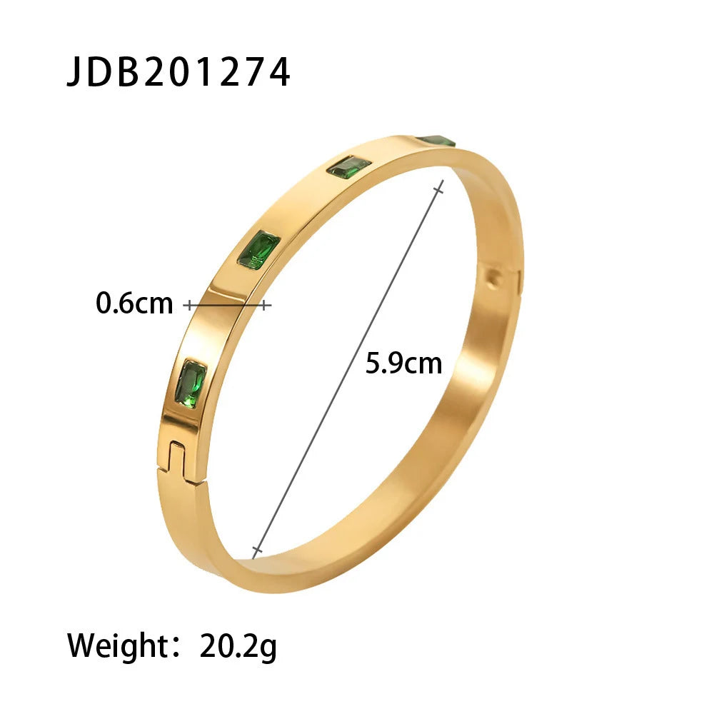 Product close-up of the Emerald Gold Hinged Bangle on a white background, showing 5.9 cm inner diameter, 0.6 cm width, and 20.2 g weight with rectangular green stones evenly spaced | Oria Jewel