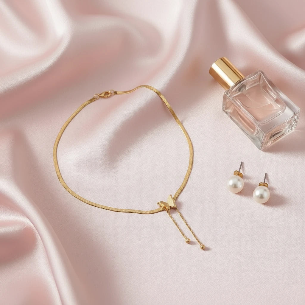 Gold Butterfly Chain Necklace placed on pink satin fabric beside perfume bottle and pearl earrings | Oria Jewel