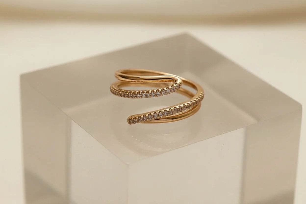 Macro product close-up of the Gold CZ Wrap Ring on a frosted acrylic cube, highlighting the elegant spiral wrap shape and pavé CZ detail against a clean neutral background | OriaJewel