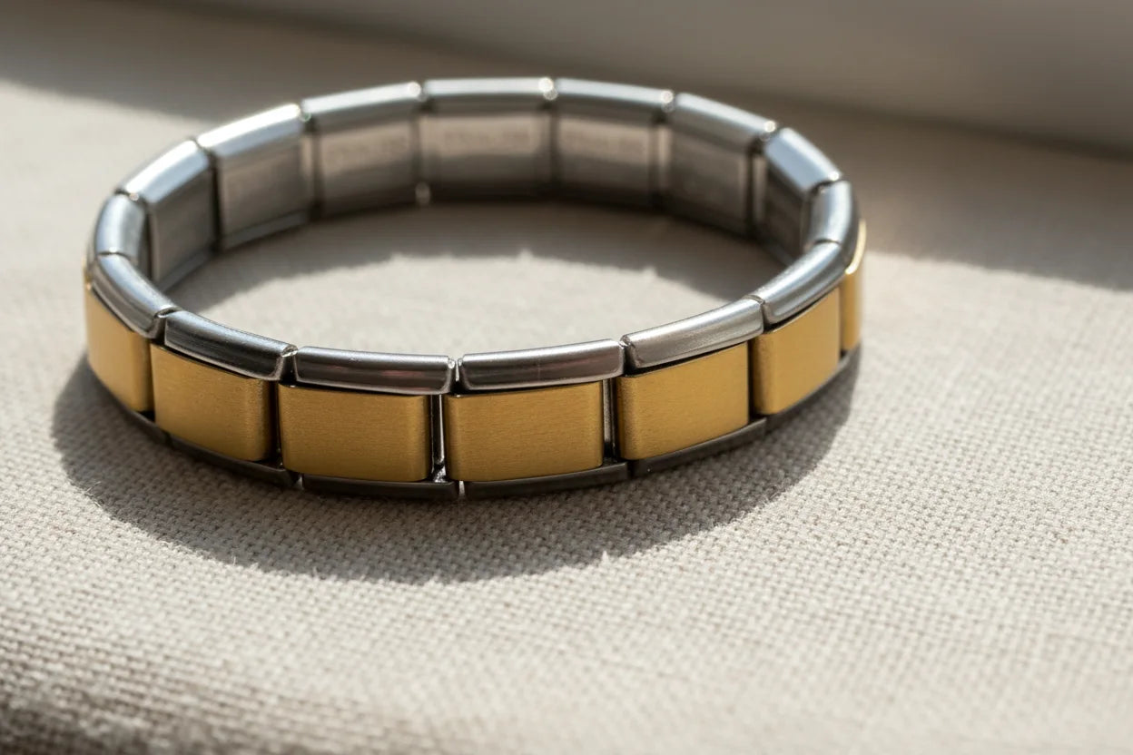 Close-up of Gold Center Stainless Steel Stretch Bracelets lying on a beige fabric surface near a window, natural daylight showcasing the smooth brushed gold segments framed by polished silver stainless steel | Oria Jewel