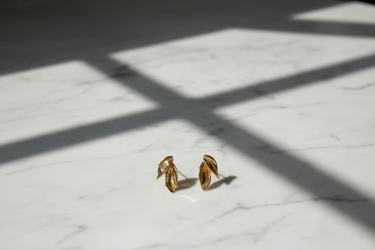 Gold Double Leaf Stud Earrings on marble surface with window light shadows | OriaJewel