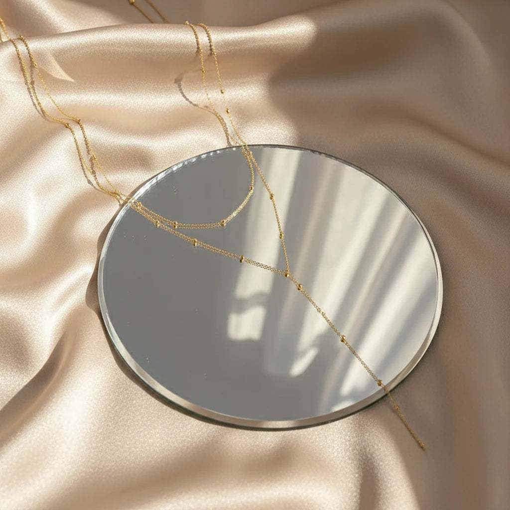Gold Drop Pendant Necklace in gold arranged on round mirror over satin fabric with soft reflections | Oria Jewel