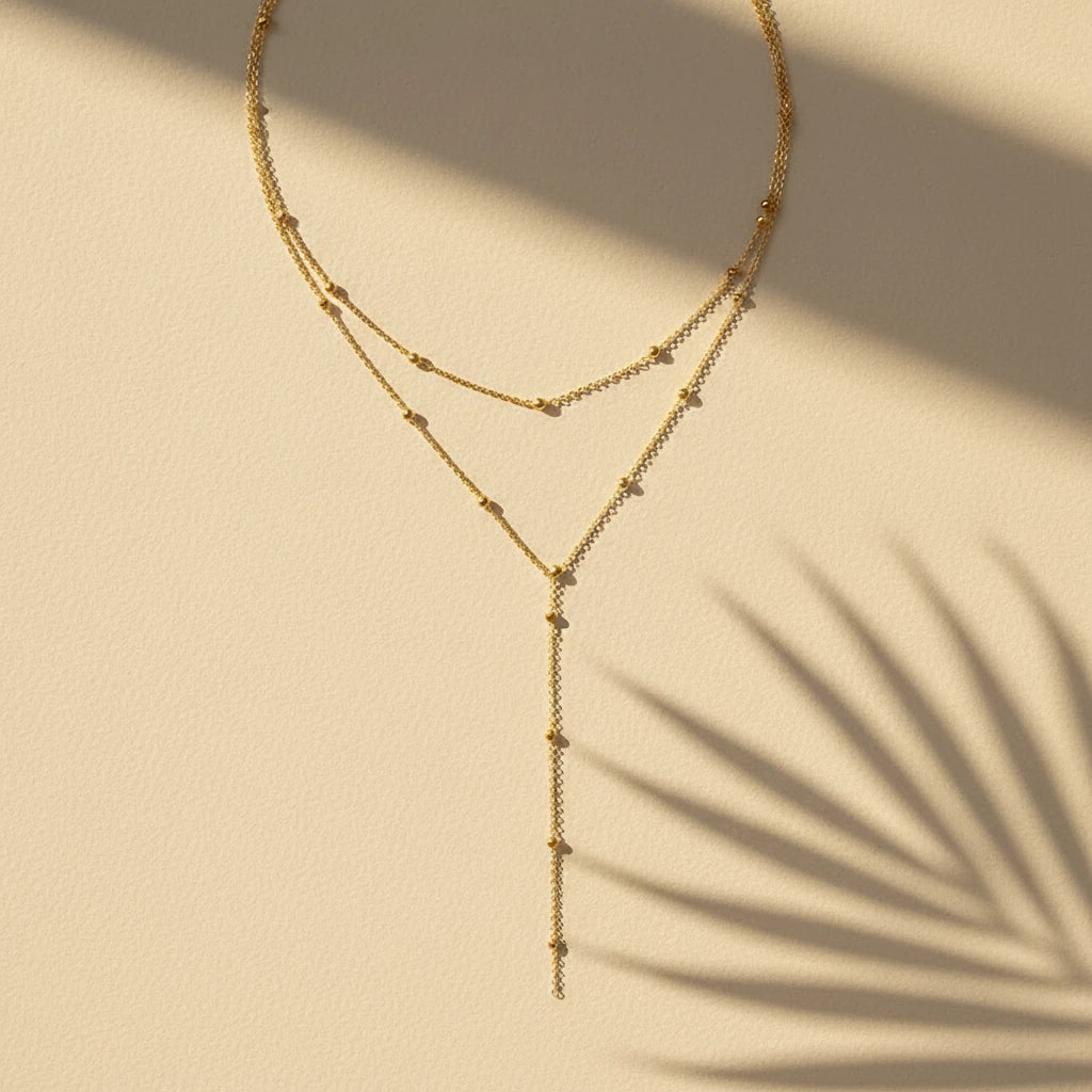 Gold Drop Pendant Necklace in gold placed on beige surface with tropical palm leaf shadows | Oria Jewel