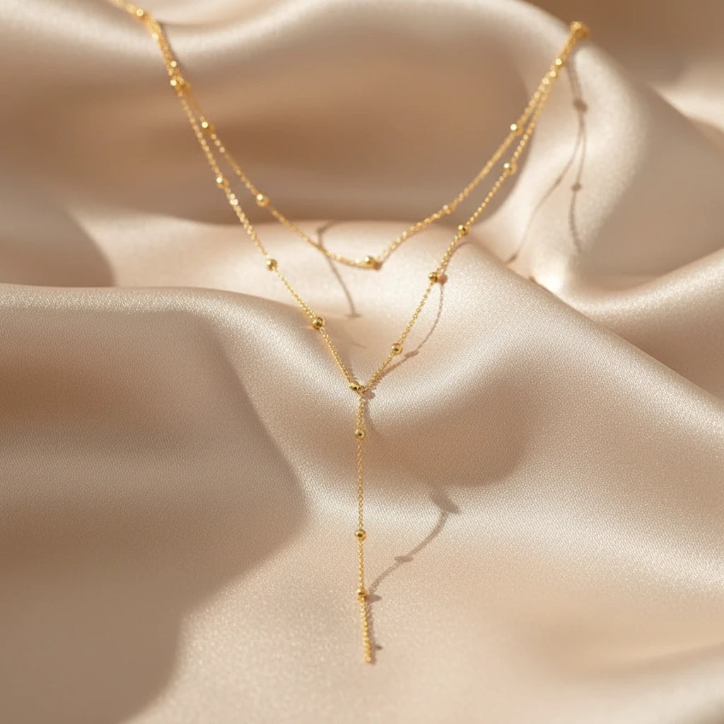 Gold Drop Pendant Necklace in gold arranged on smooth satin fabric under soft daylight reflections | Oria Jewel