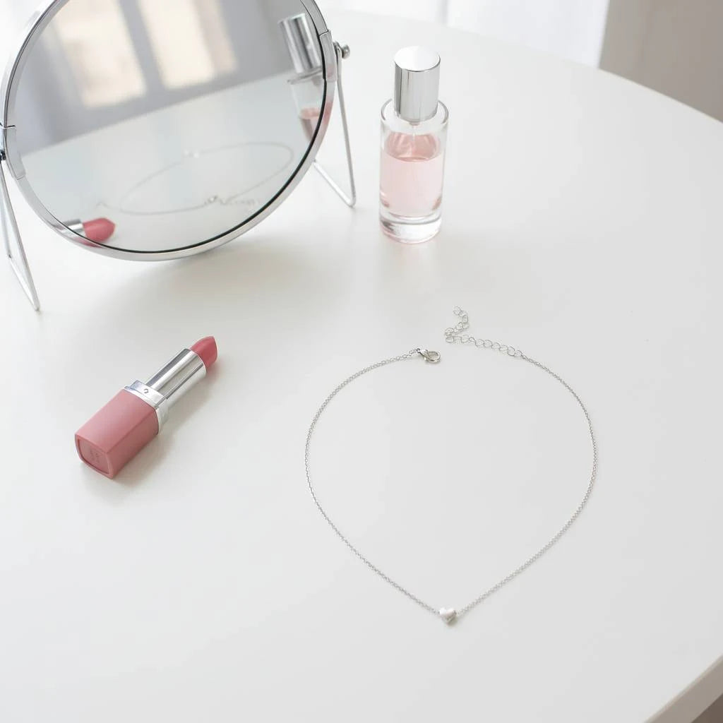 Flat lay of vanity table with mirror, perfume, lipstick and dainty Silver version of Gold Love Pendant Necklace | Oria Jewel