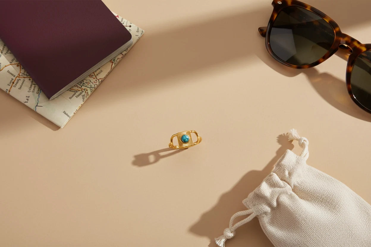 Gold Turquoise Adjustable Open Ring travel-inspired flat-lay on a warm neutral surface with a map, sunglasses, and a drawstring pouch, ring centered with crisp shadows and turquoise pop | OriaJewel