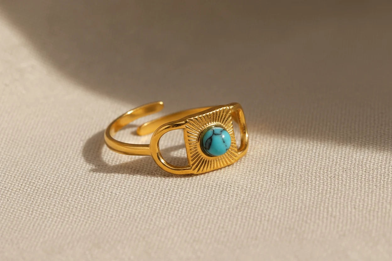 Gold Turquoise Adjustable Open Ring macro on textured beige fabric, detailed view of the turquoise cabochon and engraved sunburst pattern framed by open geometric gold sides | OriaJewel