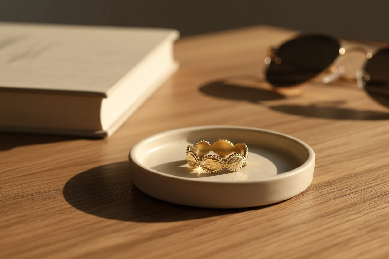Gold beaded marquise ring placed in a small ceramic dish on a wooden table, warm golden sunlight with a book and sunglasses softly out of focus | OriaJewel