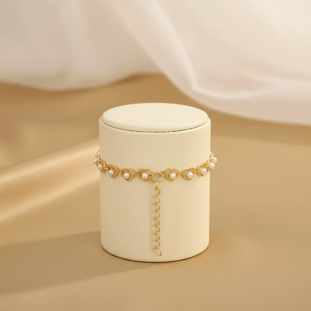 Golden Pearl Heart Chain Bracelet displayed around a cream cylindrical stand with the extender chain draping down, set against a silky golden backdrop for an elegant jewelry presentation | Oria Jewel