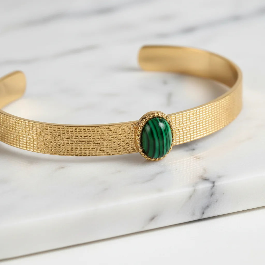 Close-up macro shot of the Green Gemstone Cuff Bracelet on a white marble surface, focusing on the detailed grid texture of the gold band and the polished oval green gemstone framed by a delicate beaded bezel | Oria Jewel