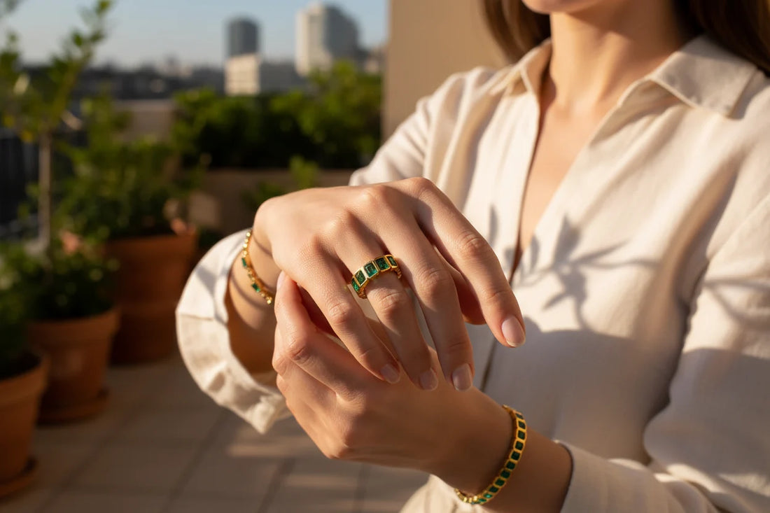 Green stone band ring on a modelโs hand outdoors at golden hour, rooftop greenery background, elegant pose highlighting the gold-tone setting and vivid green stones | OriaJewel
