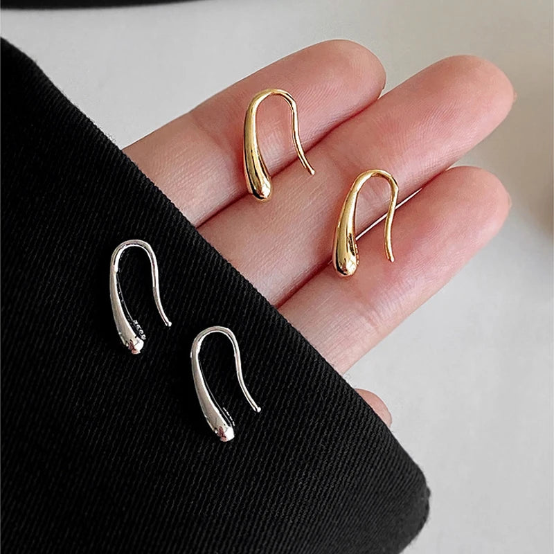 Close-up of sleek gold and sterling drop earrings on a hand | Oria Jewel