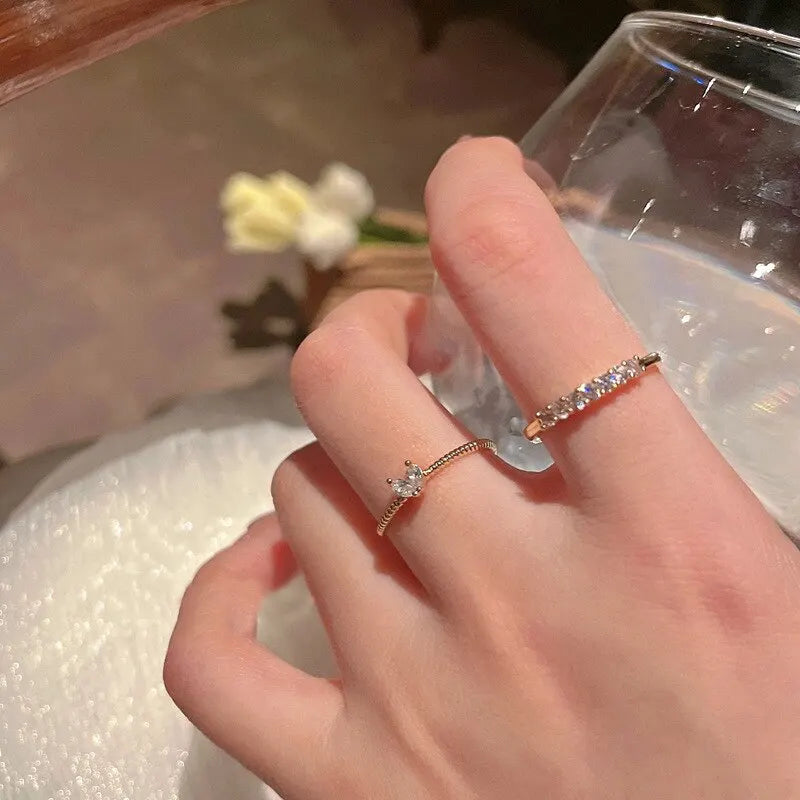 Luna Dainty Stack Ring Set worn on the hand while holding a clear glass, showing two slim gold rings—one with a small marquise cluster and one with a row of sparkling stones—in warm indoor lighting | OriaJewel