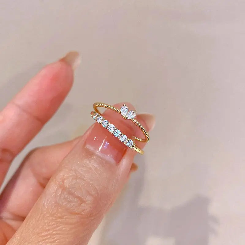 Luna Dainty Stack Ring Set held between fingers in a macro shot, highlighting the stacked look of the crystal row band and the marquise accent ring with a glossy manicure | OriaJewel