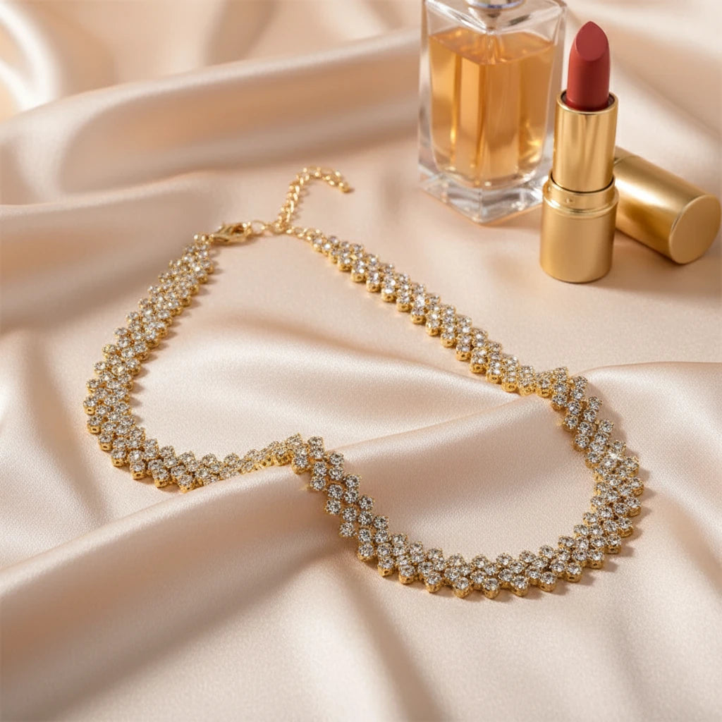 Luxury Rhinestone Chain Choker in gold tone displayed with perfume and lipstick on soft beige satin fabric | Oria Jewel