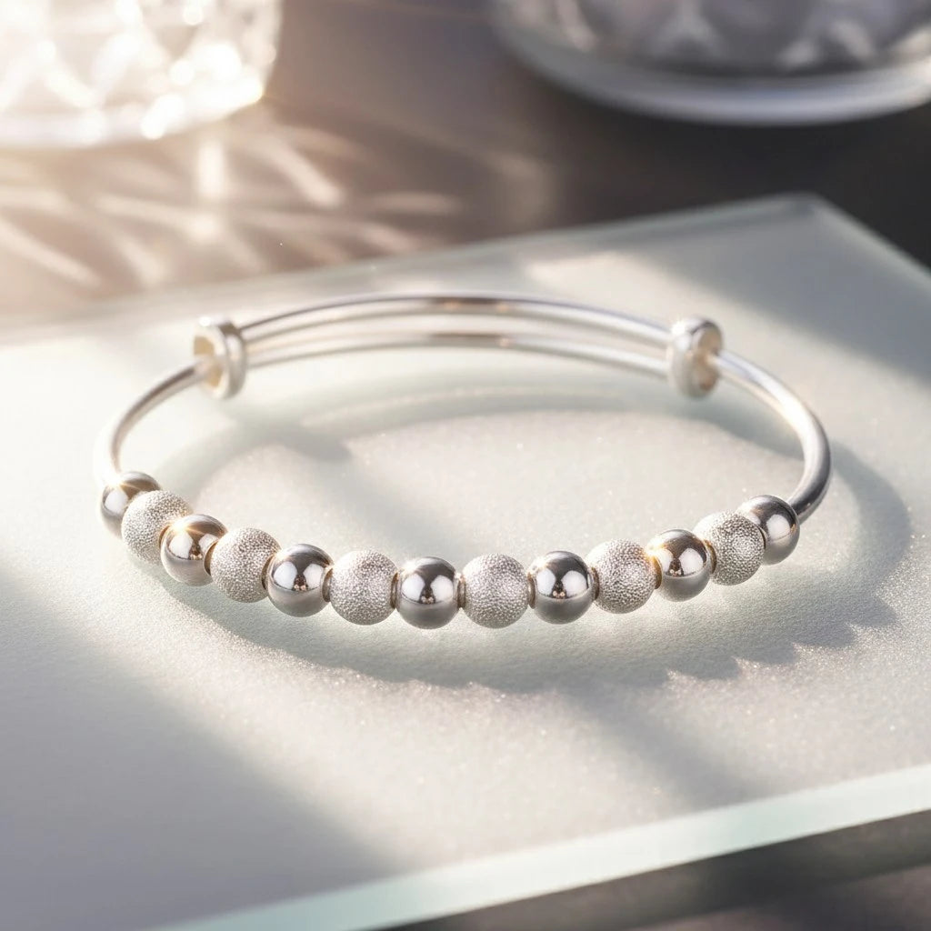 Close-up of the Marvella Beaded Charm Cuff resting on a frosted glass tray, highlighting the contrast between brushed and mirror-finish beads and the sleek silver band in natural sunlight | Oria Jewel