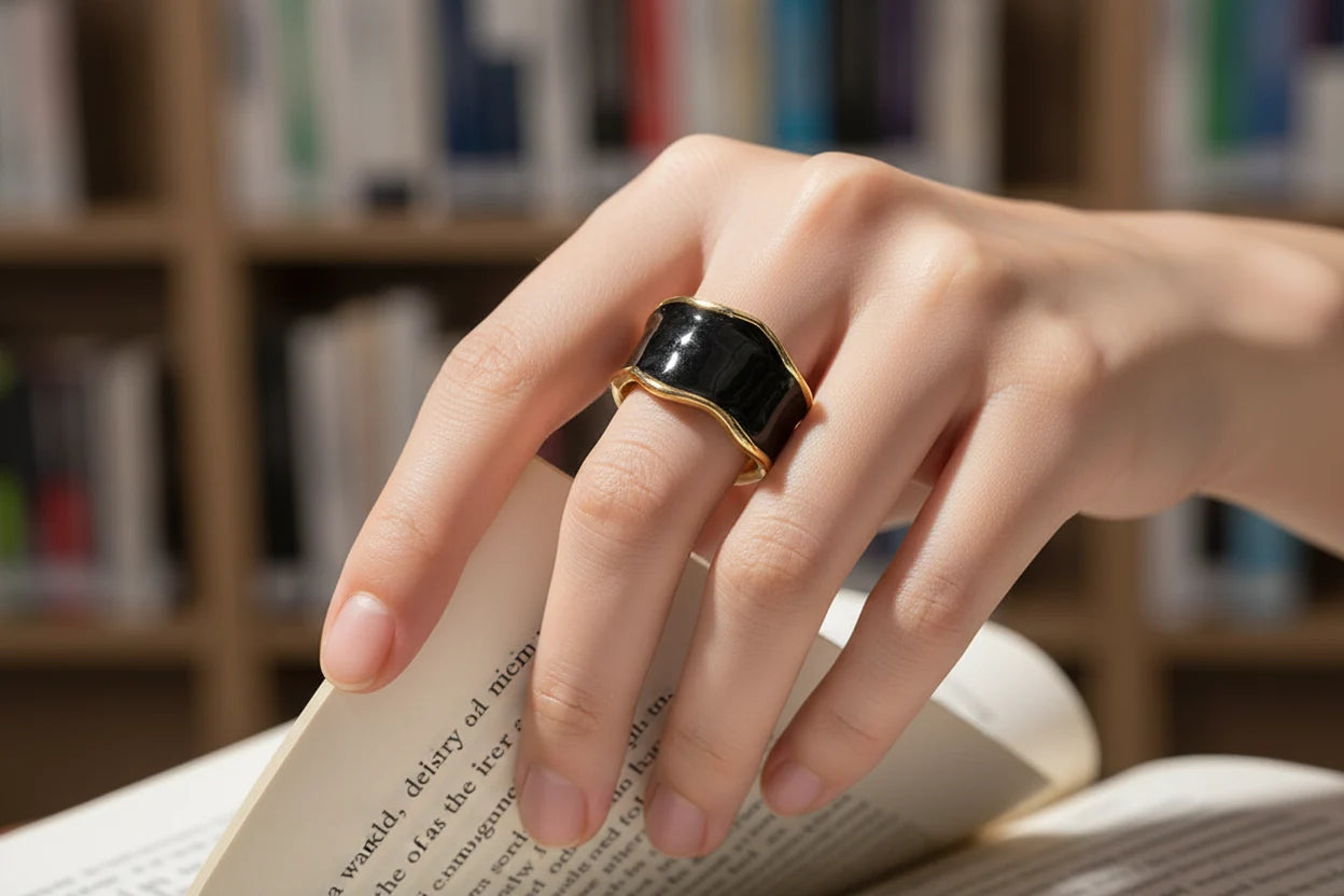 Midnight Black Open Wave Ring close-up on a hand turning pages in a book, black wavy open band with gold-trim detail against a cozy library background | OriaJewel