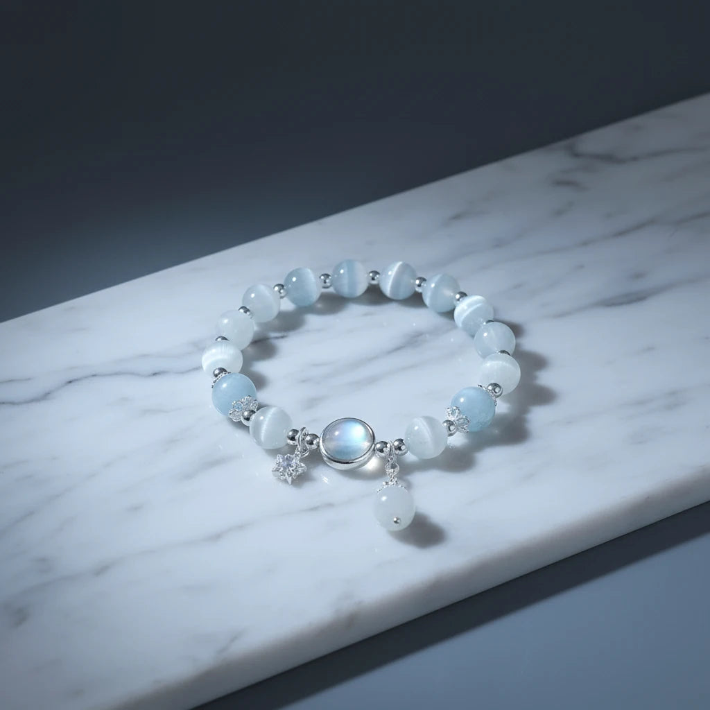 Moonstone Glow Charm Bracelet displayed on a cool marble surface, spotlighting the translucent blue beads and reflective moonstone centerpiece | Oria Jewel