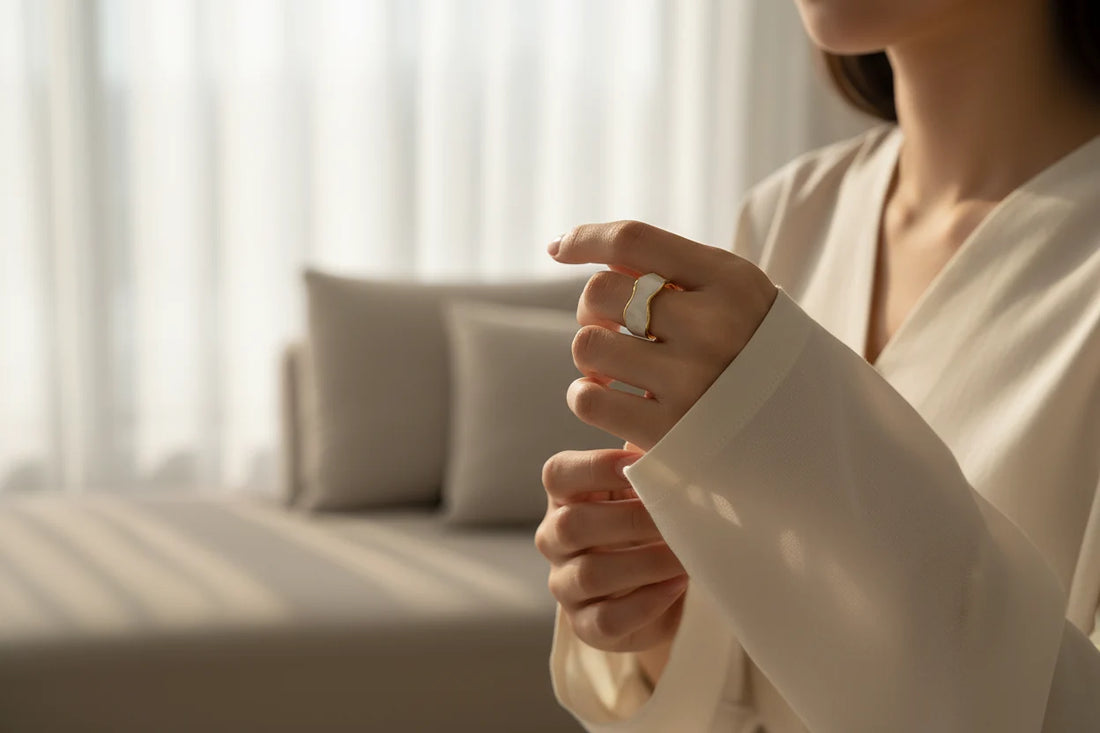 Pearl White Open Wave Ring worn in a soft lifestyle shot near a bed and sheer curtains, showing the pearl-white wave band with gold outline on a relaxed hand pose | OriaJewel