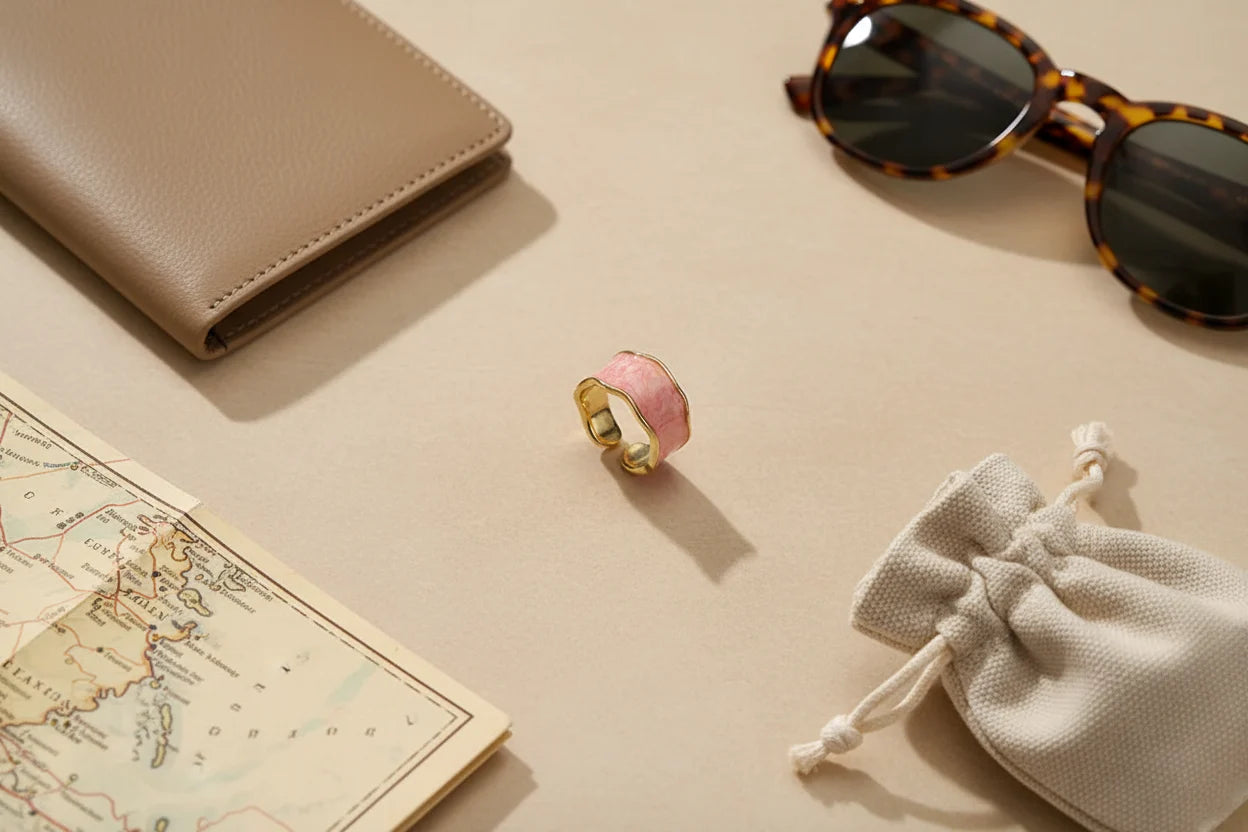Pink Marble Open Wave Ring flat-lay on a neutral desk with a travel map corner, beige wallet, tortoiseshell sunglasses, and a small drawstring pouch, warm sunlight casting soft shadows | OriaJewel