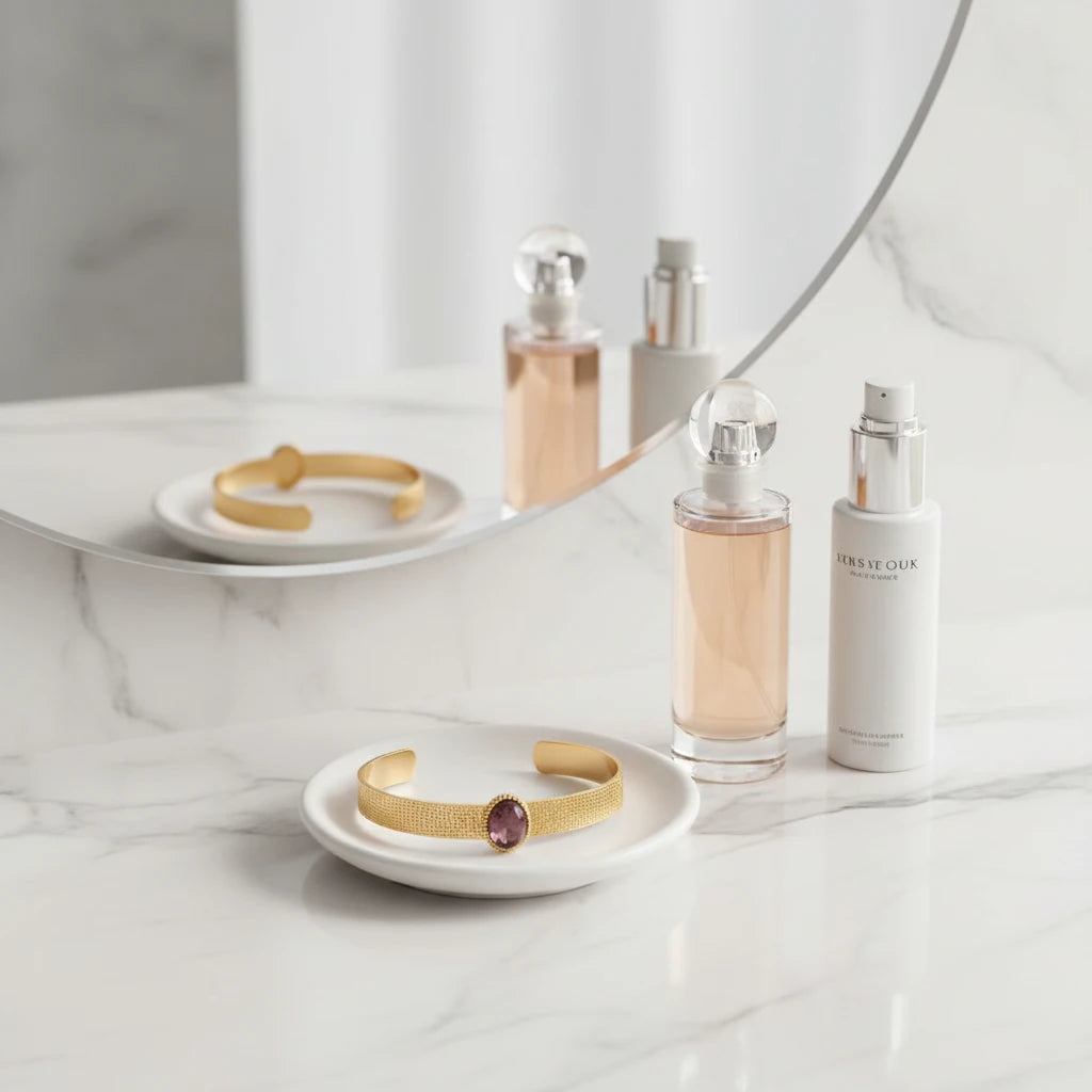 Plum gemstone cuff bracelet resting on a white ceramic dish on a marble vanity, the textured gold band and glossy plum stone styled beside elegant perfume bottles for a feminine dressing-table look. | Oria Jewel