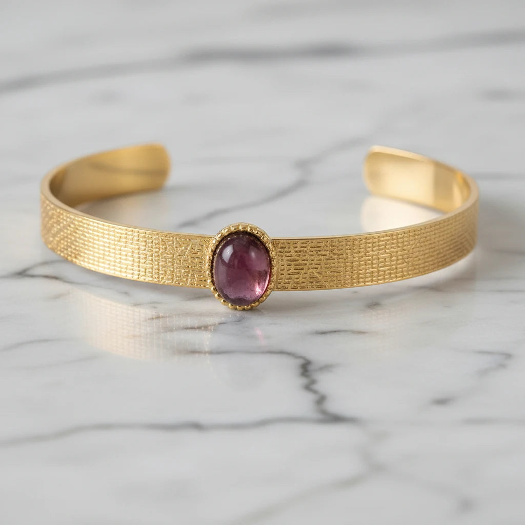 Detailed close-up of the plum gemstone cuff bracelet lying on white marble, highlighting the textured gold band and smooth oval plum stone set in a delicate beaded bezel. | Oria Jewel