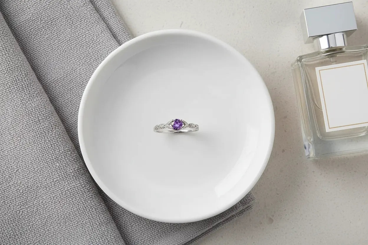 Purple Solitaire Filigree Ring centered on a white ceramic dish beside a folded gray towel and perfume bottle, clean vanity flat lay. | OriaJewel