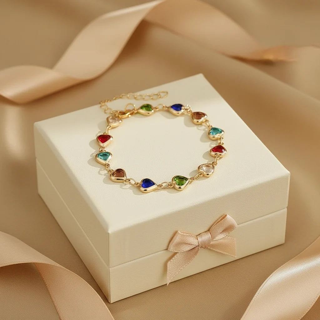 Rainbow Heart Charm Bracelet displayed in a gift box, arranged in a perfect circle of red, blue, green, turquoise and neutral heart charms with satin ribbon props | Oria Jewel