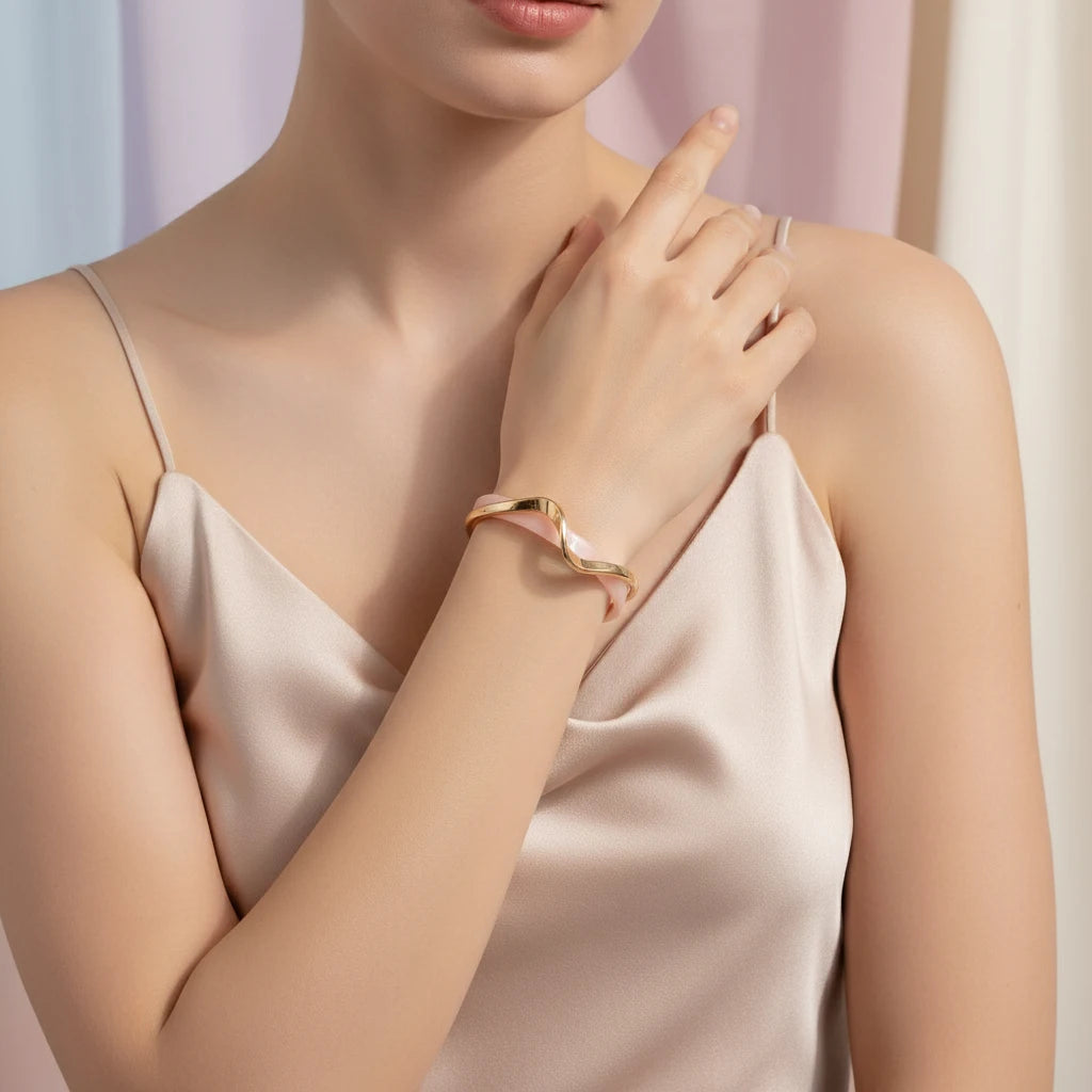 Close-up of a woman in a blush satin camisole gently touching her neck while the Rosette twist cuff bracelet curves around her wrist in soft pink and gold tones | Oria Jewel