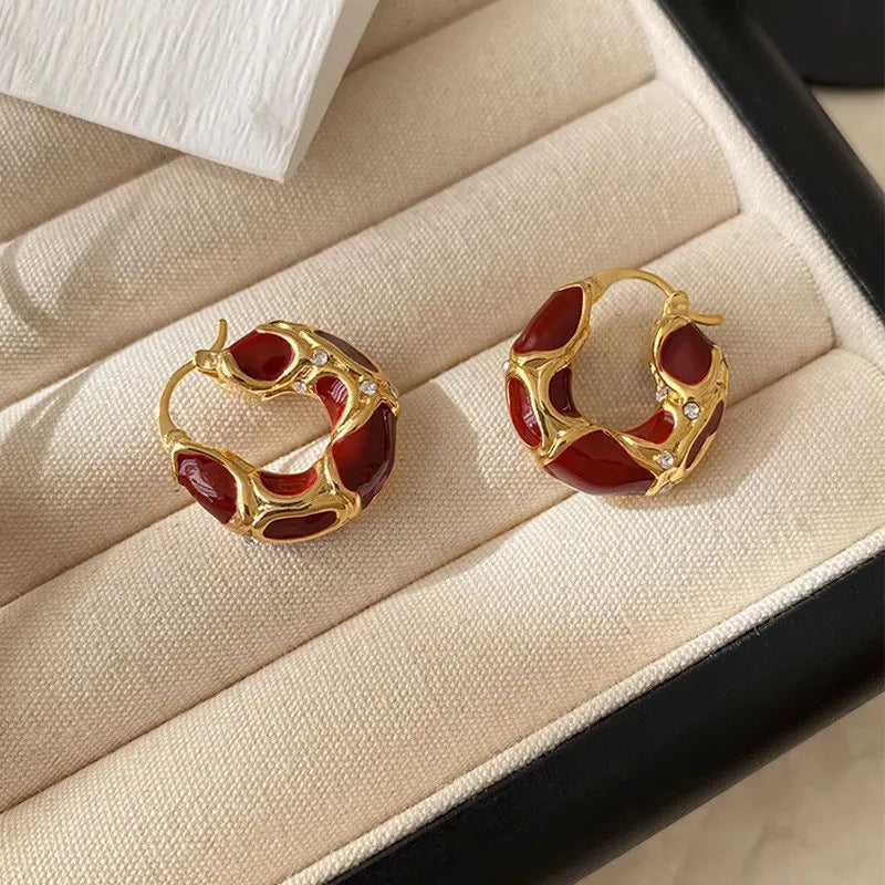 Two ornate gold and red enamel drop earrings with sparkling stones on a cream tray | Oria Jewel