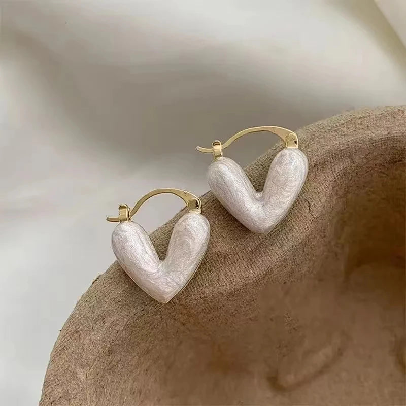 Gold and pearlescent Minimalist Heart Drop Earrings resting on brown fabric | Oria Jewel