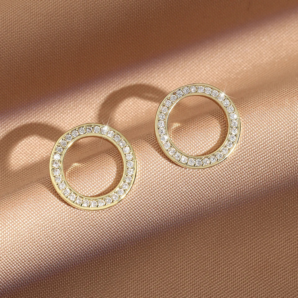 Overhead view of two shimmering gold Hollow Zircon Earrings on tan fabric | Oria Jewel