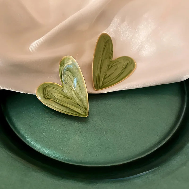 Glossy green swirled enamel heart pretty studs, gold trim, on light fabric | Oria Jewel