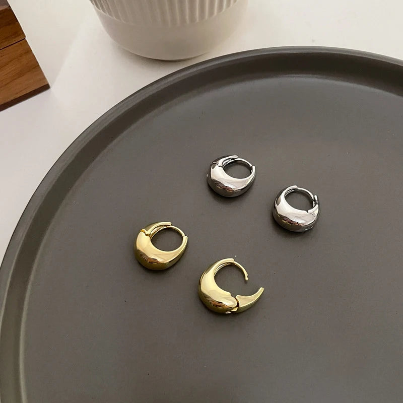 Two shiny chunky gold earrings and two silver on a dark tray | Oria Jewel