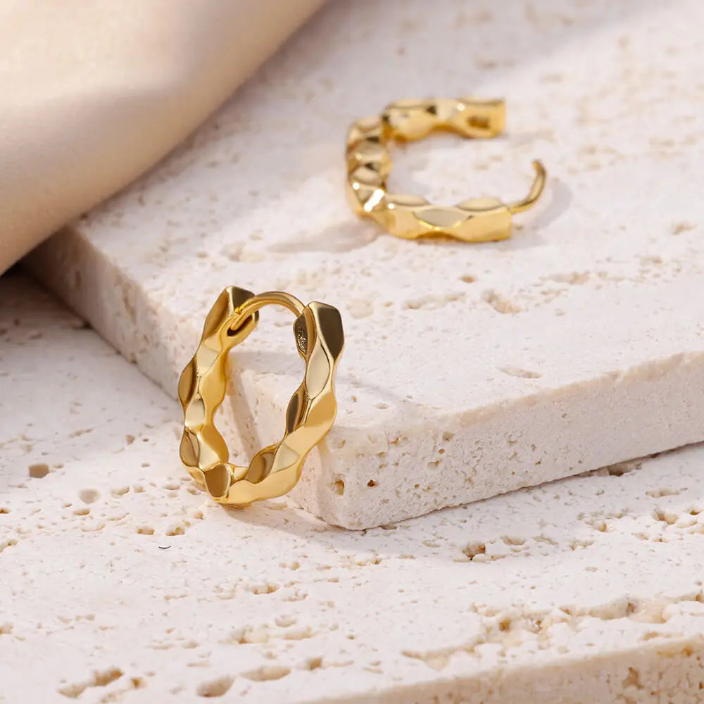 Two shiny Wavy Gold Mini Hoops reflecting on a bright white surface | Oria Jewel