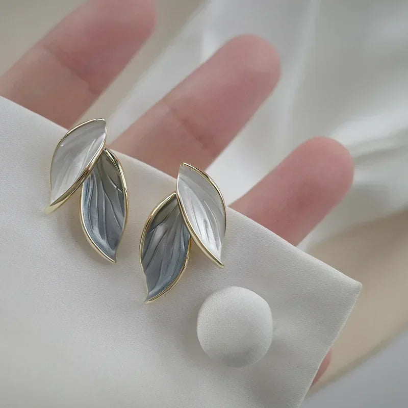Softly lit, gold-trimmed two-tone Korean Leaf Stud Earrings on white fabric | Oria Jewel