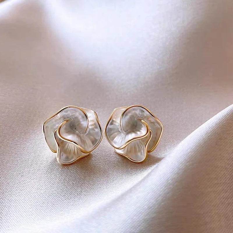 Close-up of two iridescent Camellia Flower Studs with gold trim on satin fabric | Oria Jewel