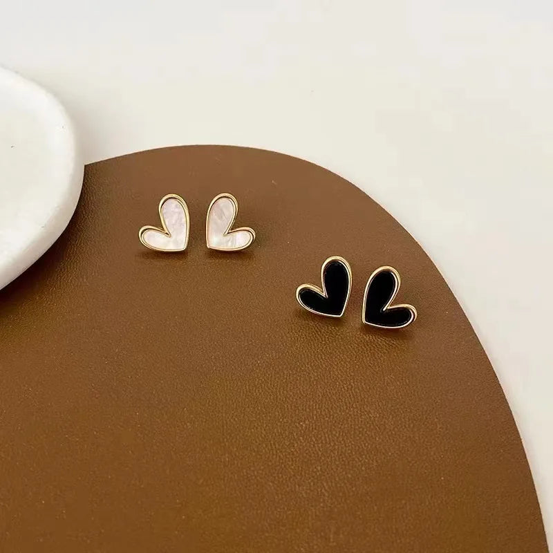 Gold-outlined white and black Mini Vintage Heart Studs on a brown textured surface | Oria Jewel