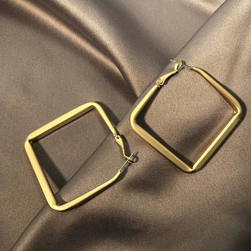 Top-down view of brushed gold diamond shape hoop earrings on dark satin | Oria Jewel
