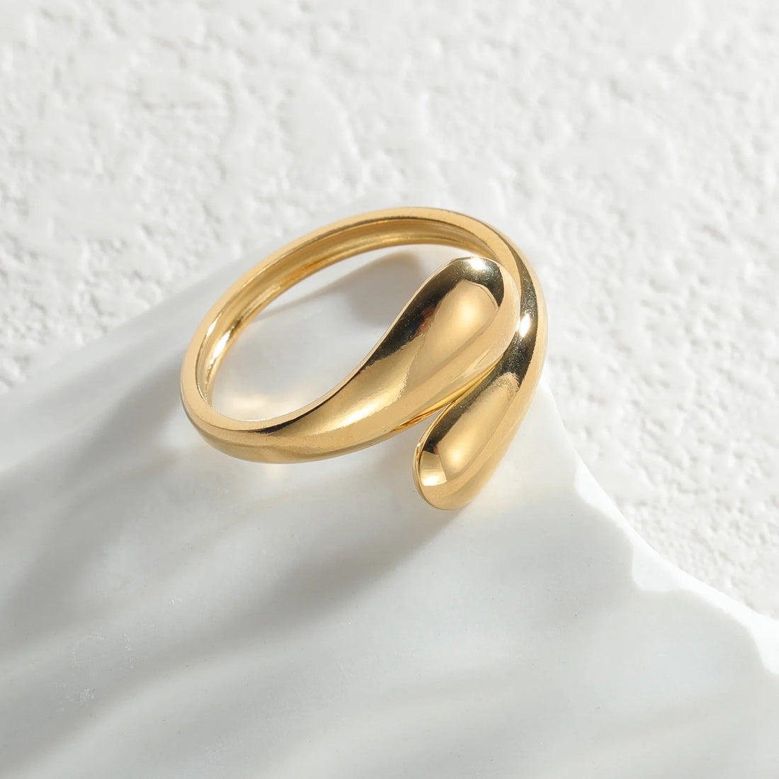 Fluid Liquid Gold Statement Ring shines on a textured white surface, close-up | Oria Jewel