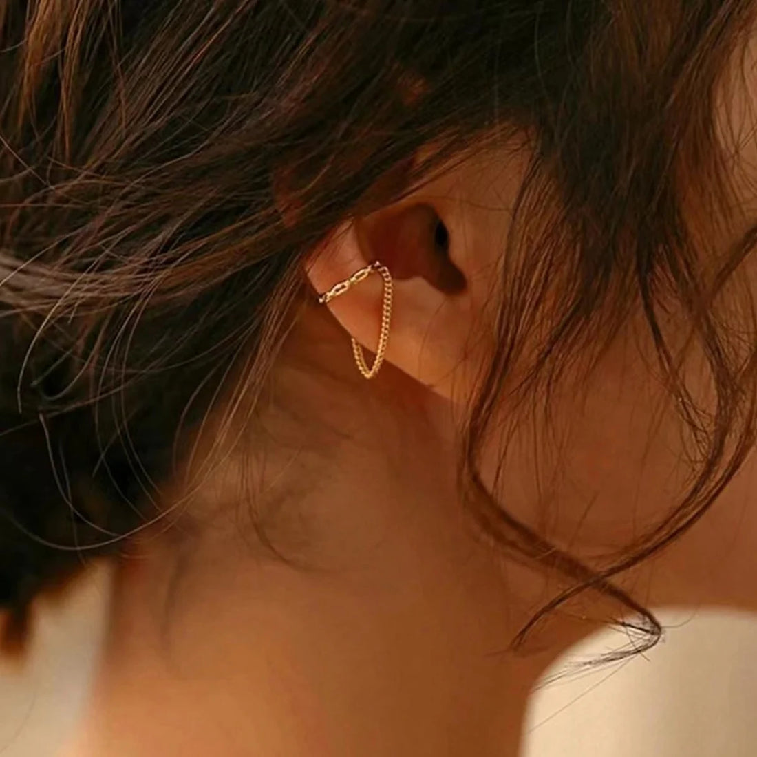 Warmly lit close-up of a Gold Clip Ear cuff with chain on ear | Oria Jewel