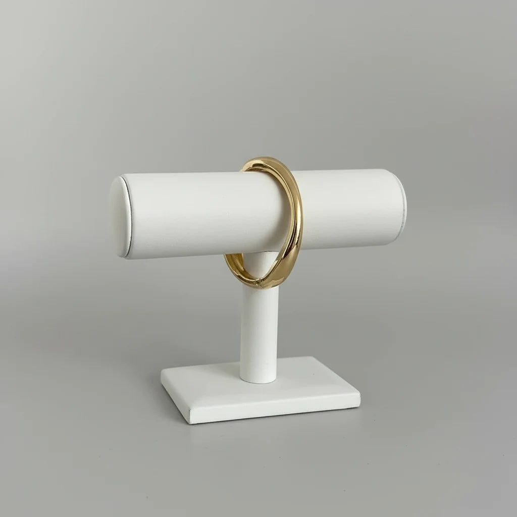 Studio close-up of the Sculpted Curve Gold Bangle displayed on a white bracelet stand, highlighting its smooth domed shape and mirror-like gold finish against a neutral background | Oria Jewel