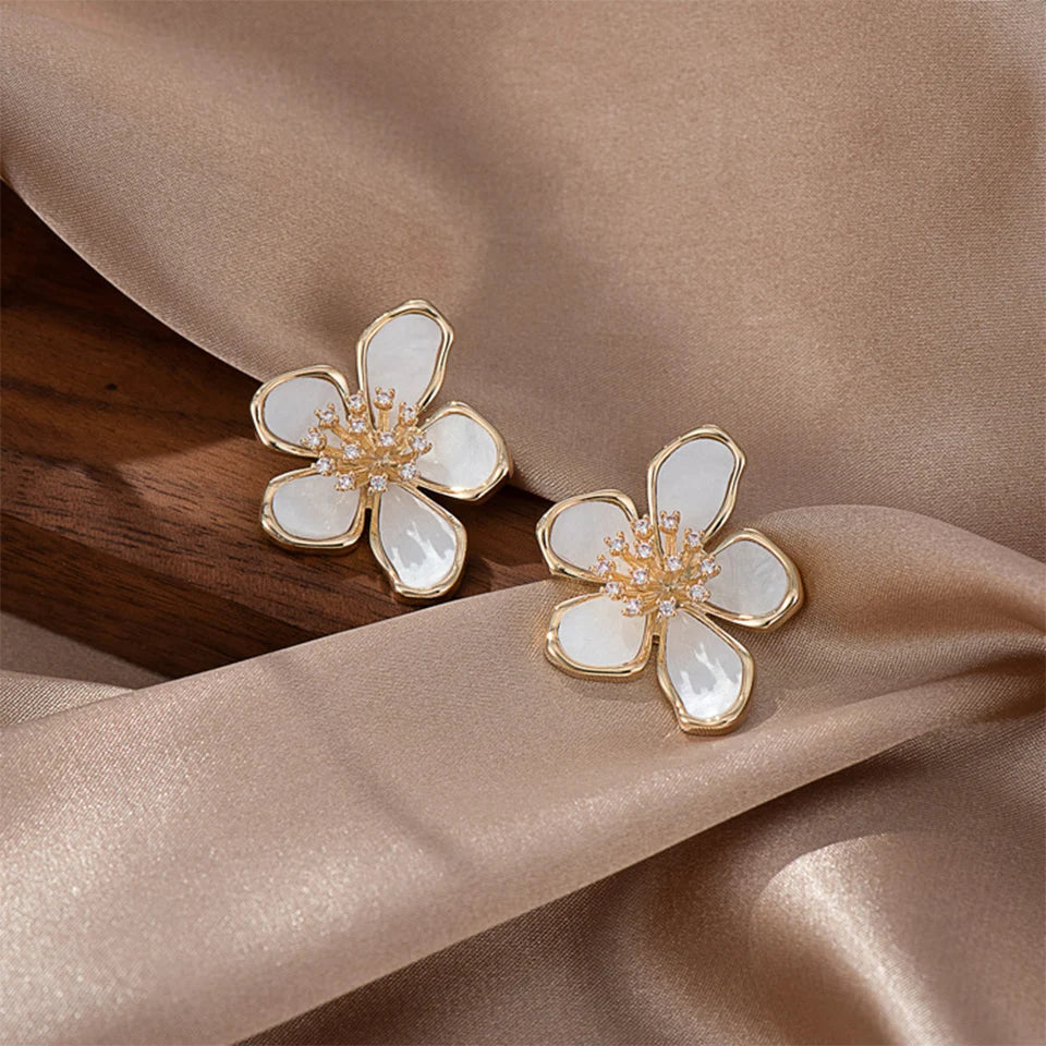 Close-up of radiant white and gold flower huggie earrings on lustrous grey satin | Oria Jewel