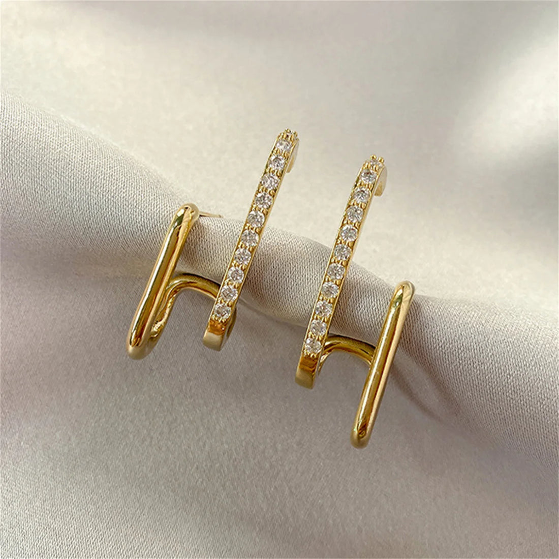 Shining double-bar gold loop hoop earrings with crystals on light fabric | Oria Jewel